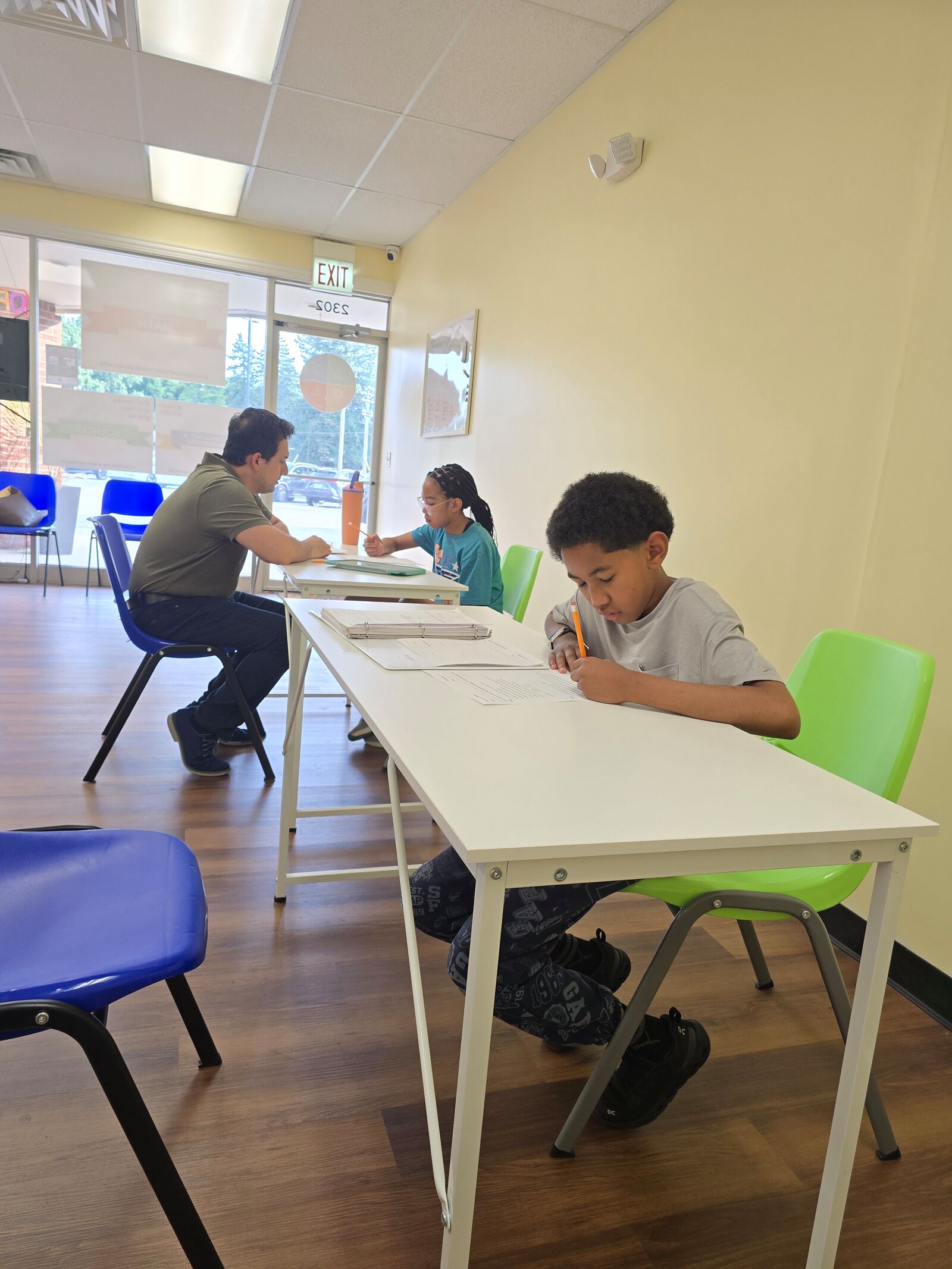 A student working through a math worksheet while a tutor helps another student